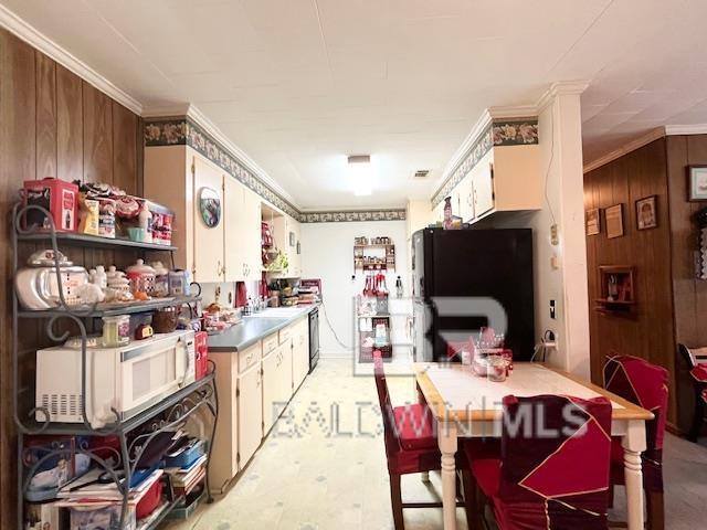 kitchen featuring white cabinets, wood walls, black fridge, and ornamental molding