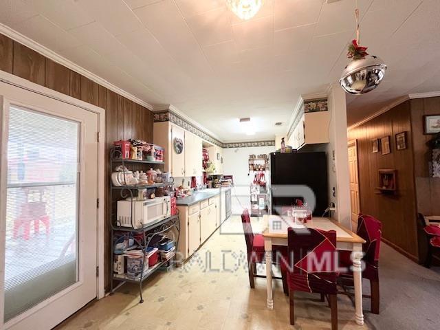 kitchen with black fridge, white cabinets, wood walls, and ornamental molding