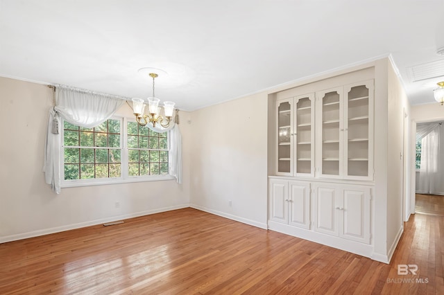 empty room featuring ornamental molding, a chandelier, and light wood-type flooring