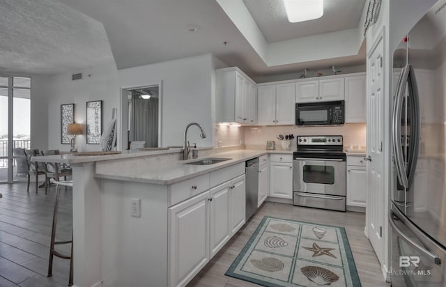 27405 Polaris St Unit 302, Orange Beach, AL 36561 - kitchen featuring stainless steel appliances, a sink, a peninsula, white cabinetry, and light wood-style flooring