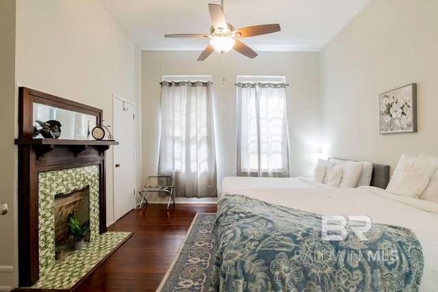 bedroom featuring ceiling fan, dark hardwood / wood-style floors, and a tiled fireplace