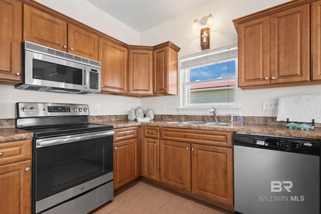 kitchen featuring light tile patterned flooring, dark countertops, brown cabinets, stainless steel appliances, and a sink