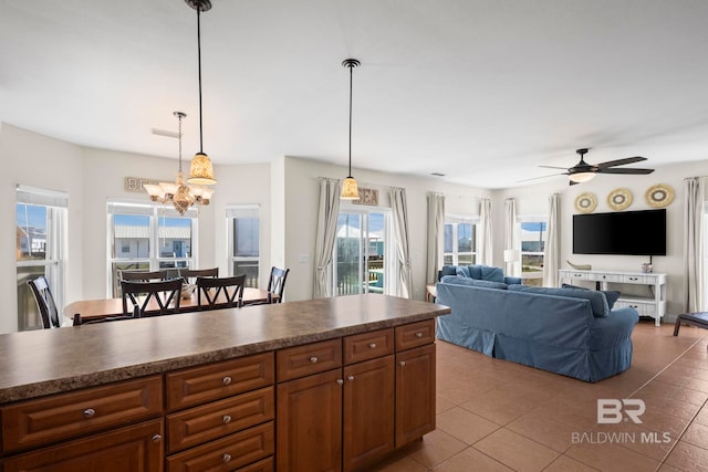 kitchen featuring dark countertops, brown cabinetry, pendant lighting, ceiling fan with notable chandelier, and tile patterned floors
