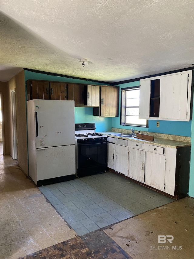 kitchen with light countertops, a sink, freestanding refrigerator, range with gas stovetop, and white cabinets