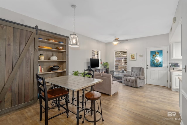 dining room featuring ceiling fan, a barn door, and light hardwood / wood-style floors