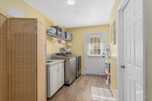 clothes washing area with light hardwood / wood-style floors, cabinets, a textured ceiling, and independent washer and dryer