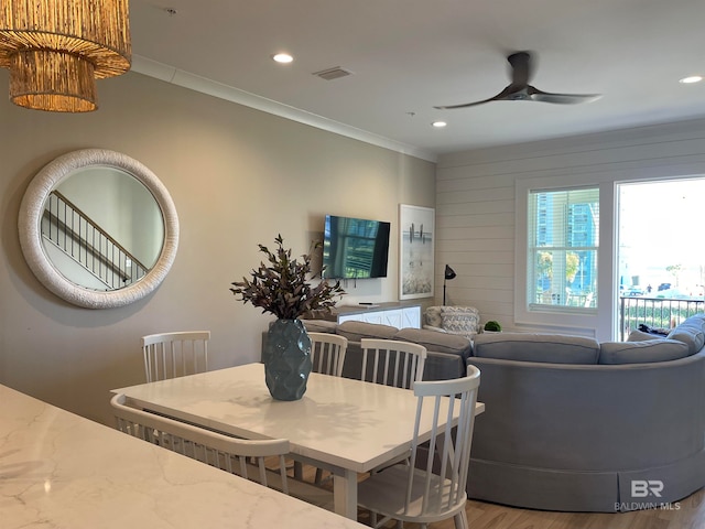 dining space with ceiling fan, wood-type flooring, ornamental molding, and wooden walls