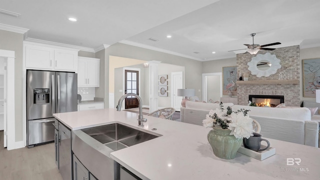 kitchen with a fireplace, sink, white cabinets, stainless steel fridge with ice dispenser, and crown molding