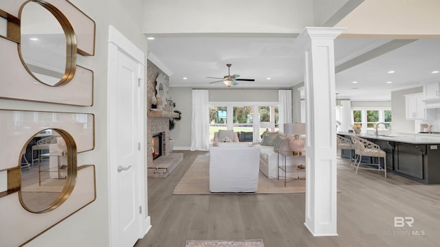 living room with decorative columns, a large fireplace, ceiling fan, light hardwood / wood-style floors, and crown molding