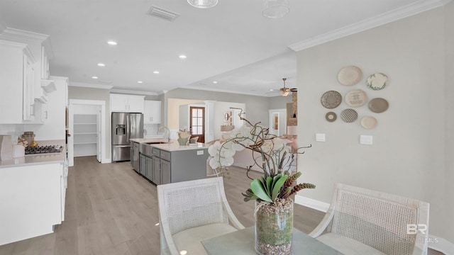 dining space featuring ceiling fan, ornamental molding, sink, and light wood-type flooring