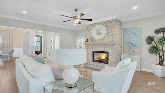 living room featuring a brick fireplace, crown molding, ornate columns, and light wood-type flooring