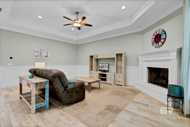 living area with a brick fireplace, a raised ceiling, and wood finished floors