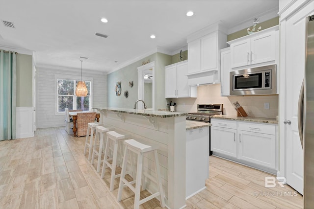 kitchen featuring stainless steel appliances, light wood-style flooring, wainscoting, and visible vents