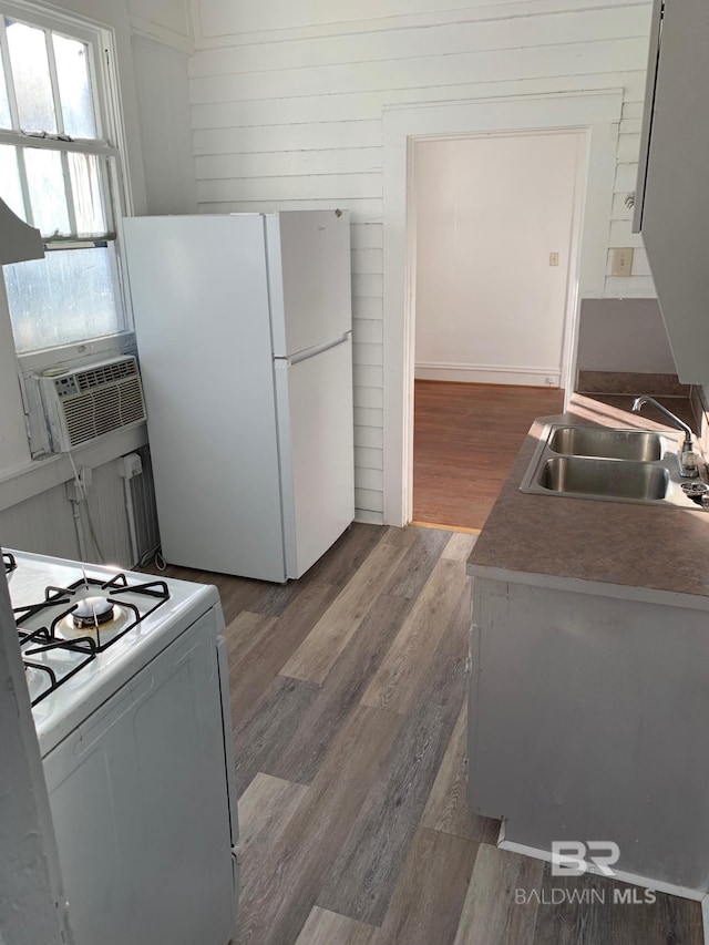 kitchen with wood finished floors, a sink, cooling unit, radiator heating unit, and white appliances