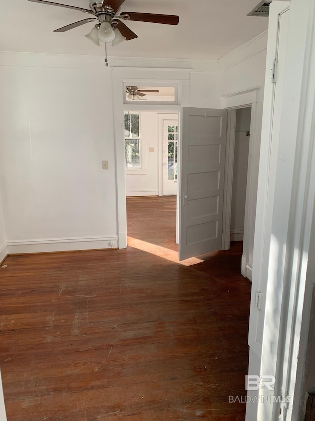 spare room with ceiling fan, baseboards, wood finished floors, visible vents, and ornamental molding