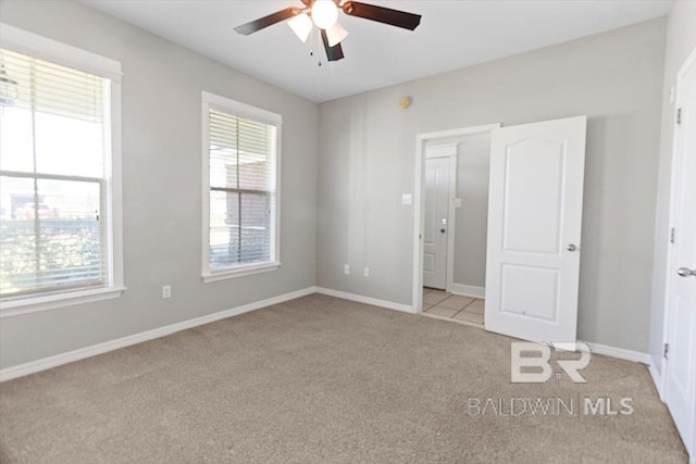 unfurnished bedroom with a ceiling fan, light colored carpet, multiple windows, and baseboards