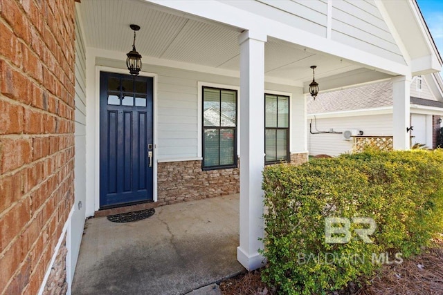 view of exterior entry featuring covered porch, stone siding, and brick siding