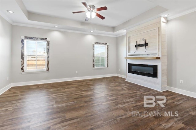 unfurnished living room featuring baseboards, a fireplace, a tray ceiling, and dark wood finished floors