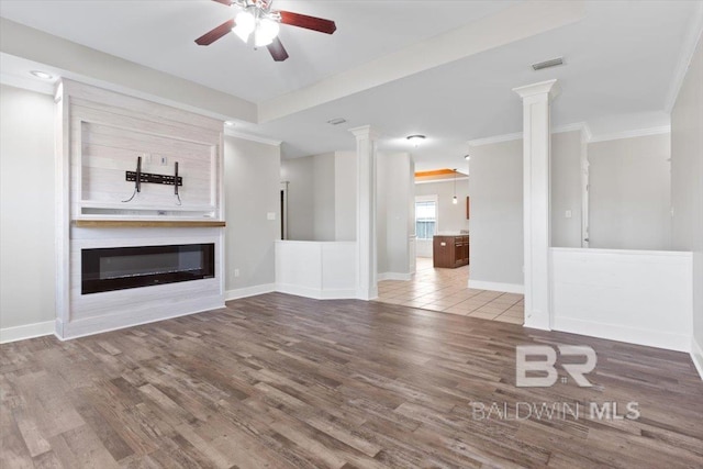 unfurnished living room featuring a glass covered fireplace, visible vents, decorative columns, and ceiling fan