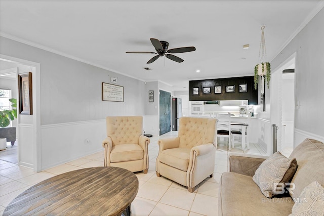 living room featuring light tile patterned floors, visible vents, ornamental molding, a ceiling fan, and wainscoting