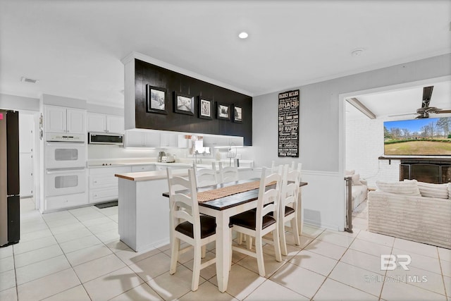 dining area with light tile patterned floors, visible vents, ceiling fan, brick wall, and crown molding