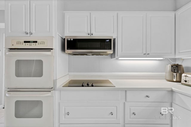 kitchen with light countertops, stainless steel microwave, double oven, white cabinets, and black electric cooktop