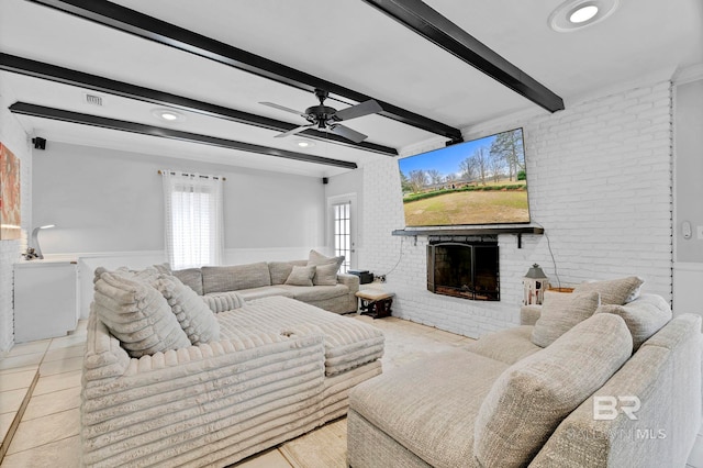 tiled living room with a ceiling fan, a brick fireplace, wainscoting, brick wall, and beamed ceiling