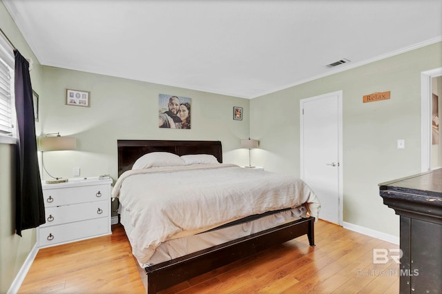 bedroom featuring ornamental molding, light wood-type flooring, visible vents, and baseboards