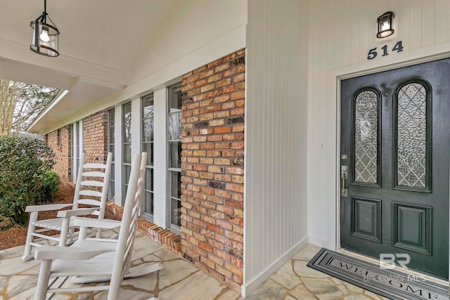 entrance to property featuring a porch and brick siding