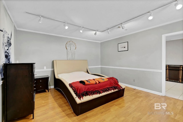 bedroom with ornamental molding, rail lighting, baseboards, and wood finished floors