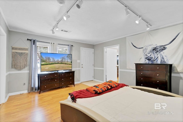 bedroom with rail lighting, crown molding, visible vents, and wood finished floors