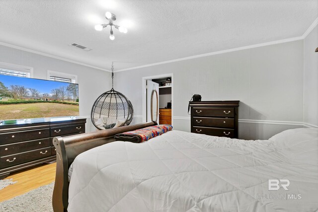 bedroom featuring a textured ceiling, wood finished floors, visible vents, ornamental molding, and freestanding refrigerator