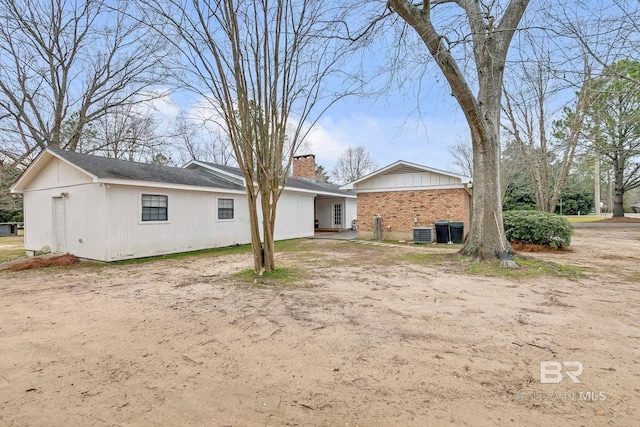 back of property featuring brick siding, a chimney, and central air condition unit