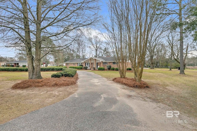 view of front of home with brick siding, driveway, a chimney, and a front lawn