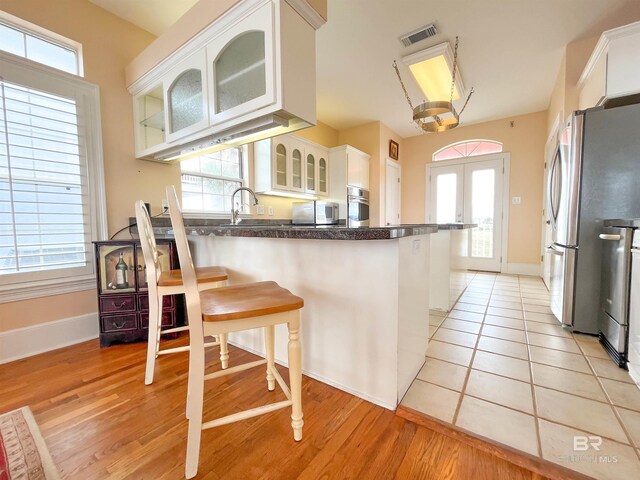 2210 W Beach Blvd, Gulf Shores, AL 36542 - kitchen featuring visible vents, a peninsula, stainless steel appliances, dark countertops, and white cabinetry