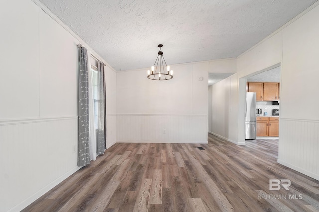 unfurnished dining area featuring a chandelier, a textured ceiling, wainscoting, and wood finished floors