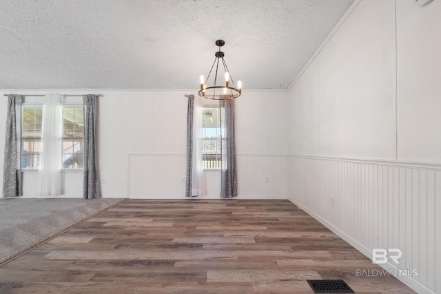 unfurnished room featuring a textured ceiling, visible vents, a chandelier, and wood finished floors