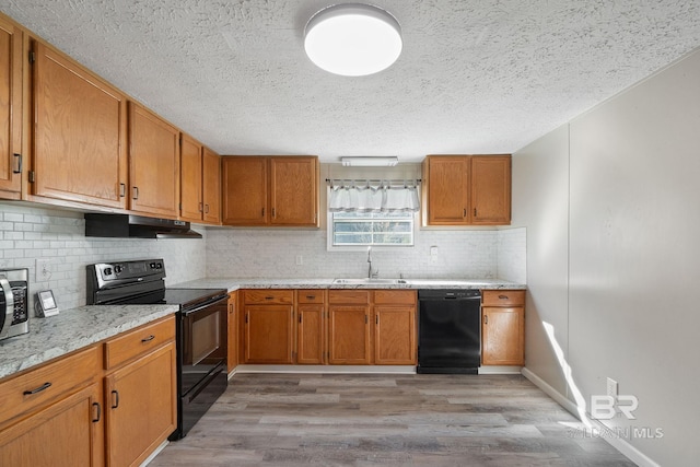 kitchen featuring black appliances, under cabinet range hood, brown cabinets, and a sink