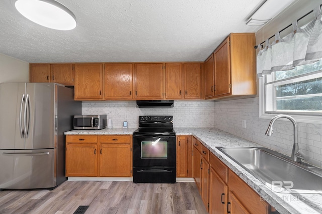 kitchen featuring brown cabinets, appliances with stainless steel finishes, a sink, light wood-type flooring, and extractor fan