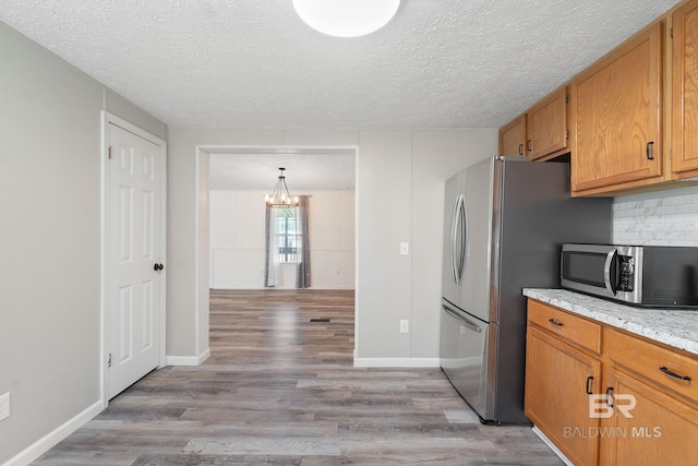 kitchen with a textured ceiling, stainless steel appliances, light wood-type flooring, tasteful backsplash, and brown cabinetry