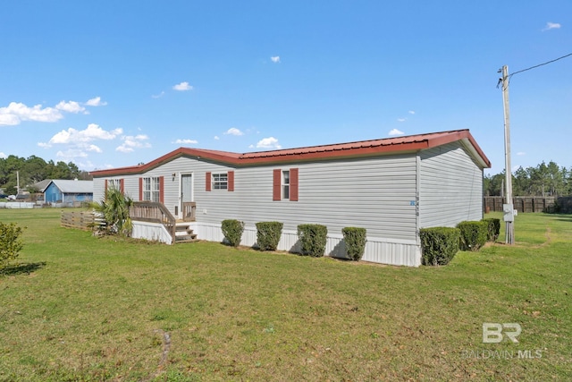 rear view of property with fence, metal roof, and a yard