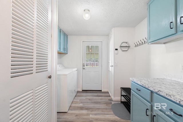 laundry room featuring washer and clothes dryer, cabinet space, light wood-style floors, a textured ceiling, and baseboards