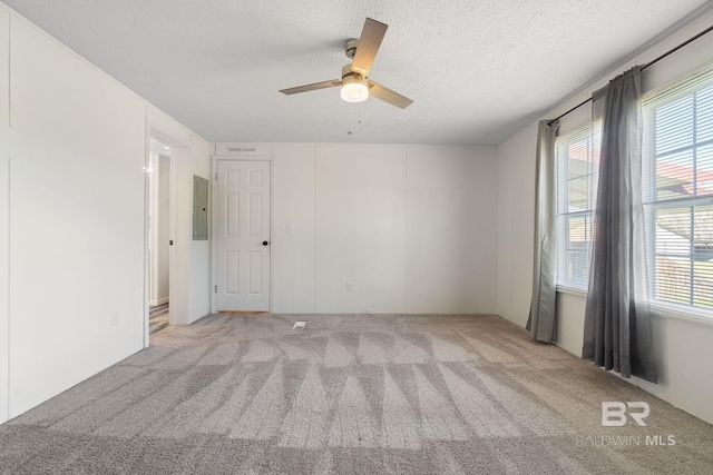 carpeted spare room with electric panel, a ceiling fan, and a textured ceiling