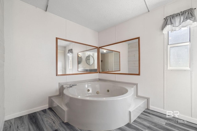 bathroom with a jetted tub, a textured ceiling, baseboards, and wood finished floors