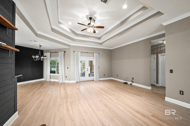 unfurnished living room featuring light wood-type flooring, ceiling fan with notable chandelier, a tray ceiling, and crown molding