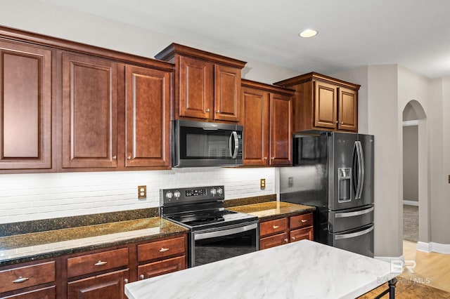 kitchen with light wood-type flooring, backsplash, dark stone countertops, and stainless steel appliances