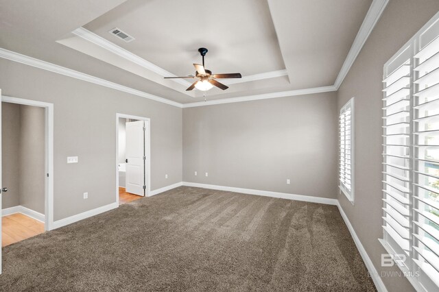 unfurnished bedroom featuring a raised ceiling, crown molding, ensuite bathroom, and carpet