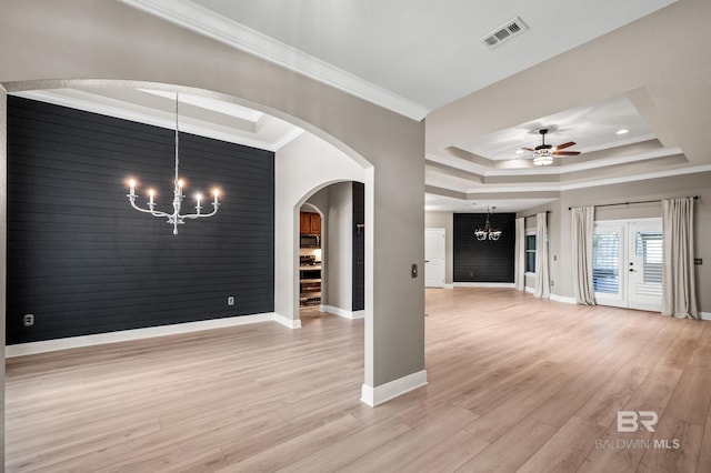 unfurnished living room with ornamental molding, ceiling fan with notable chandelier, light wood-type flooring, and a tray ceiling