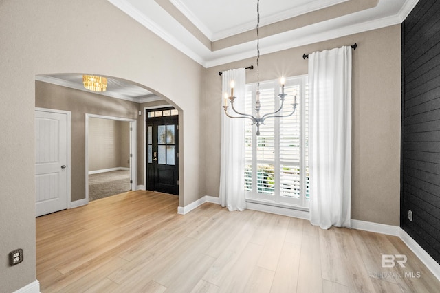 interior space featuring a notable chandelier, light hardwood / wood-style flooring, a raised ceiling, and ornamental molding