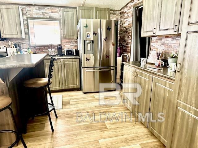 kitchen with stainless steel refrigerator with ice dispenser, a breakfast bar, a center island, light wood-type flooring, and a textured ceiling